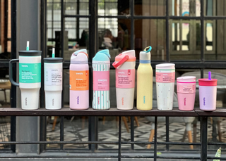 Colorful insulated tumblers on a metal railing with a blurred indoor background